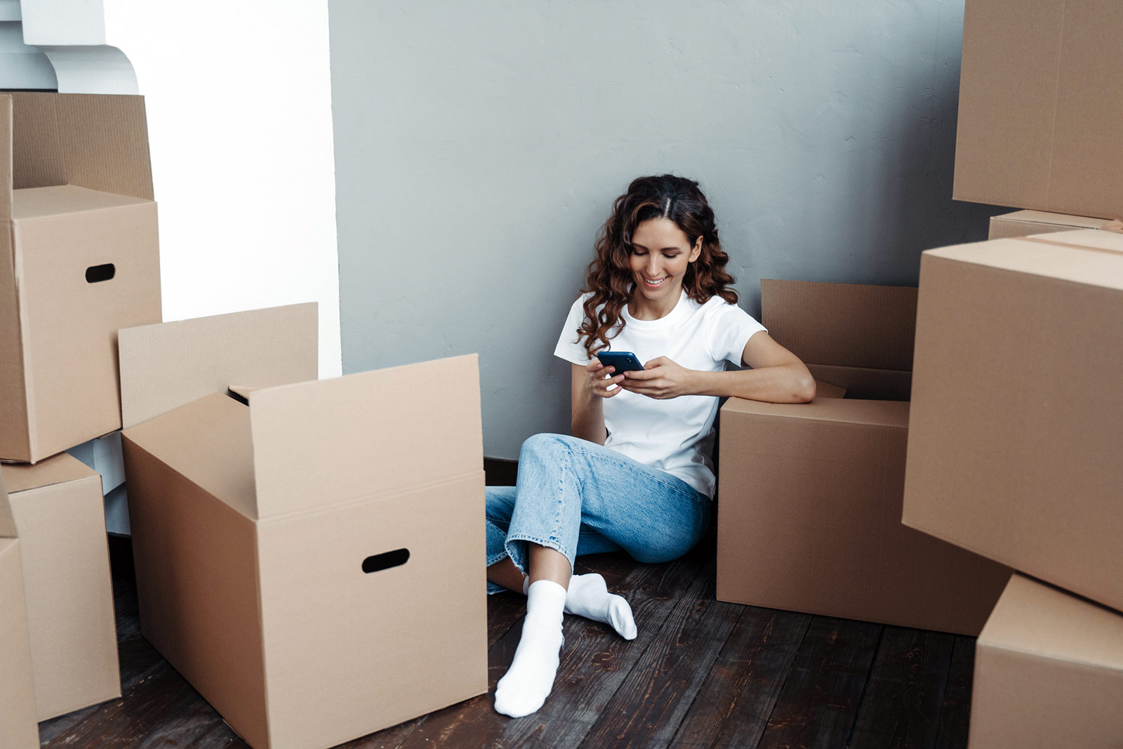 Women sitting on the ground Internet Subway Wi-Fi on her phone move-in day in her apartment, surrounded by moving boxes.